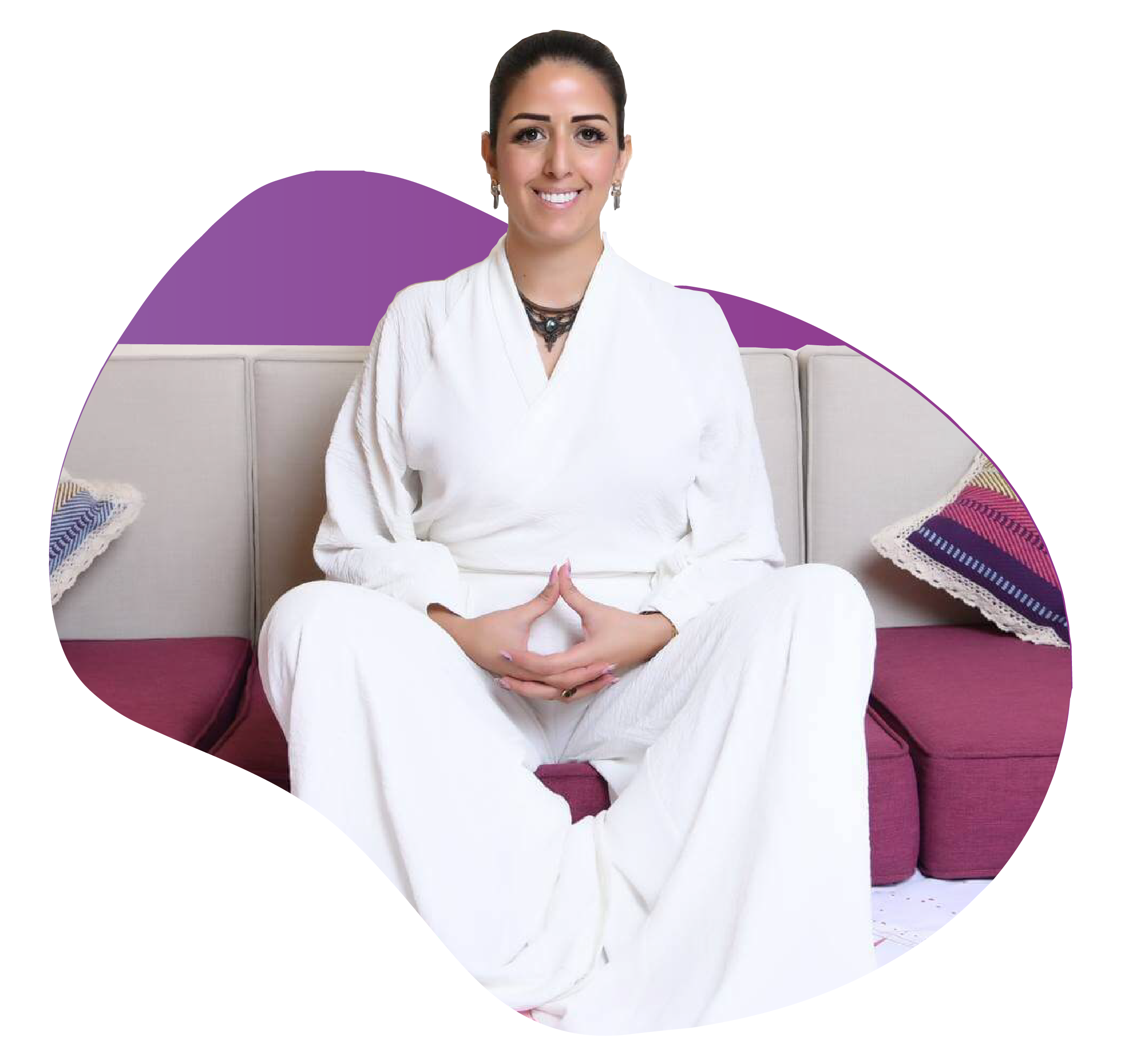 Woman in white loungewear sitting cross‑legged on a sofa with hands clasped